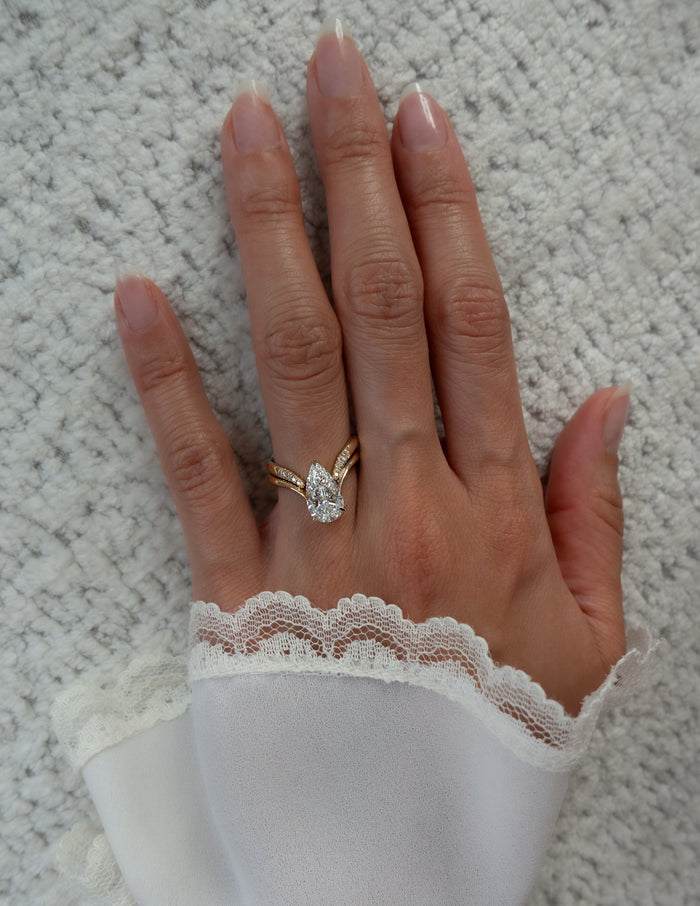 Pear lab grown diamond V ring and pave-tipped chevron band worn on a hand resting on a knit throw