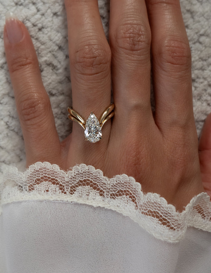 Pear lab grown diamond V ring stacked with a plain gold chevron band on a hand over lace