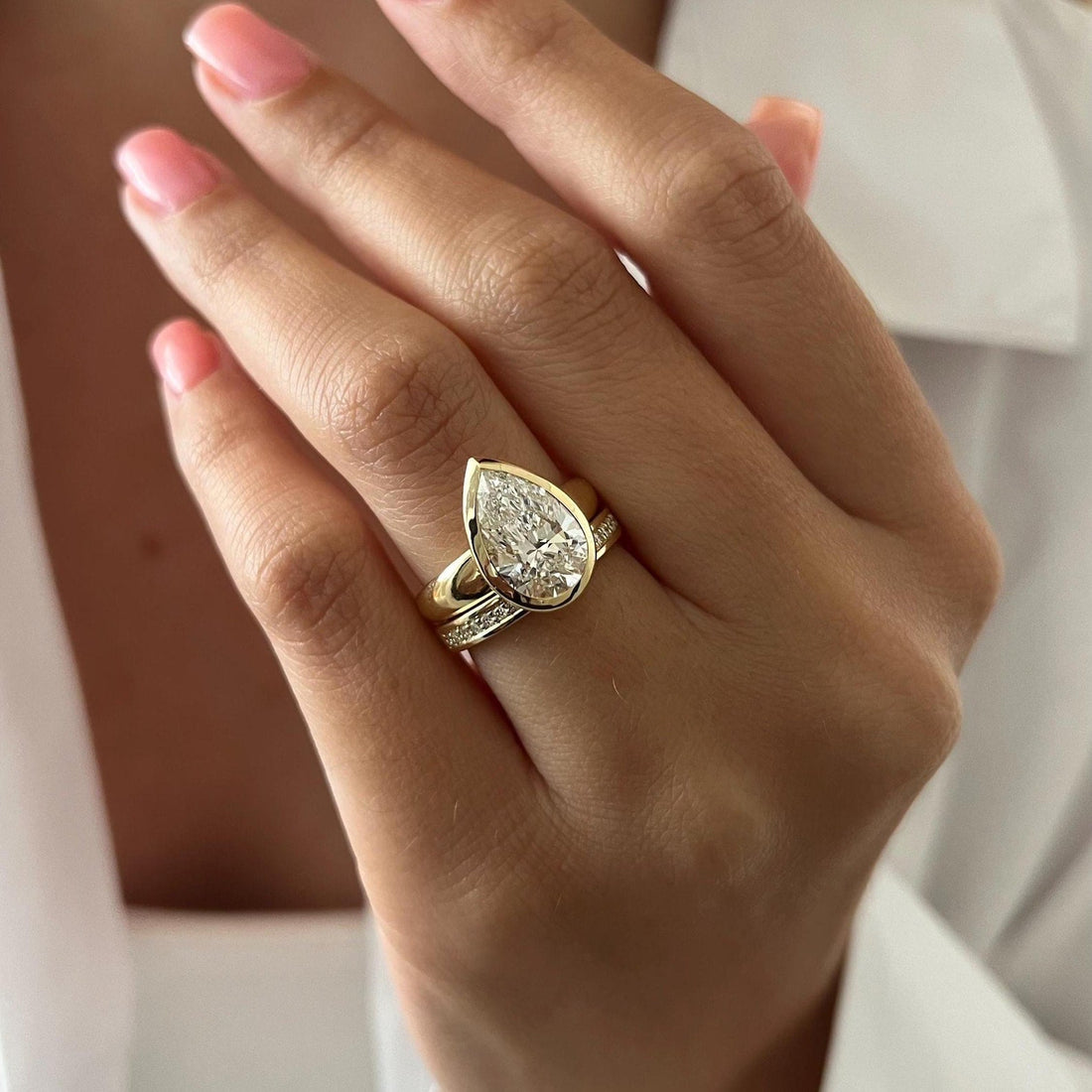 Pear moissanite bezel solitaire with channel set band in yellow gold worn on the hand