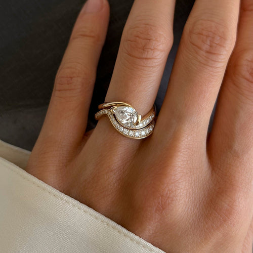 East-west pear moissanite swirl bridal set in yellow gold with graduated pave wave band worn on the hand