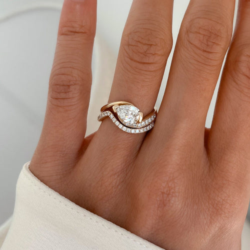 East-west pear moissanite swirl bridal set with slim curved pave band in yellow gold worn on the hand