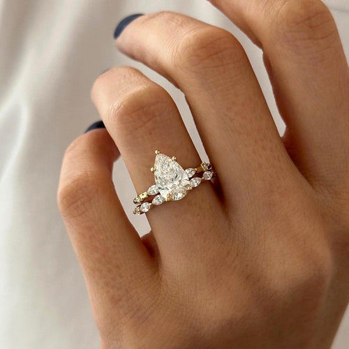 Pear moissanite bridal set with marquise accents in yellow gold worn on the hand