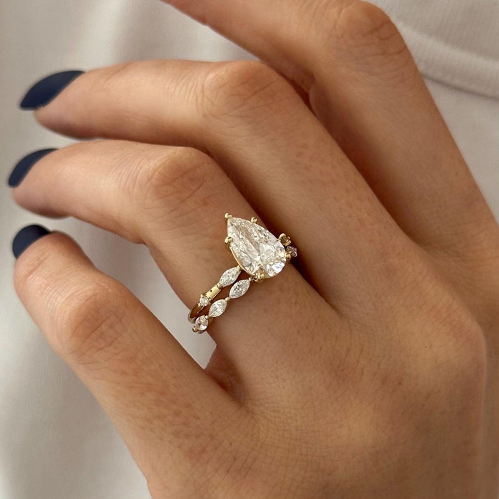 Angled view of pear moissanite engagement ring and marquise station band on the finger