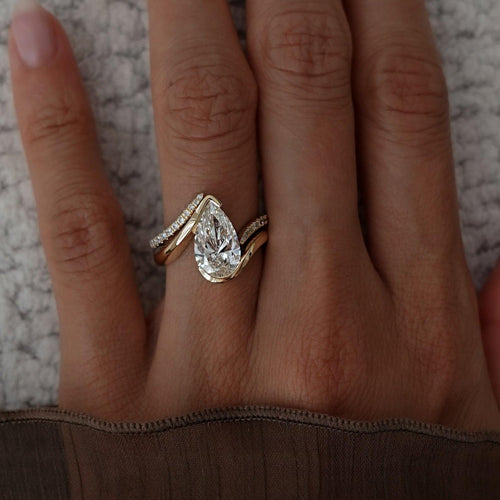 Pear moissanite swirl bridal set with chevron pave band in yellow gold worn on the hand