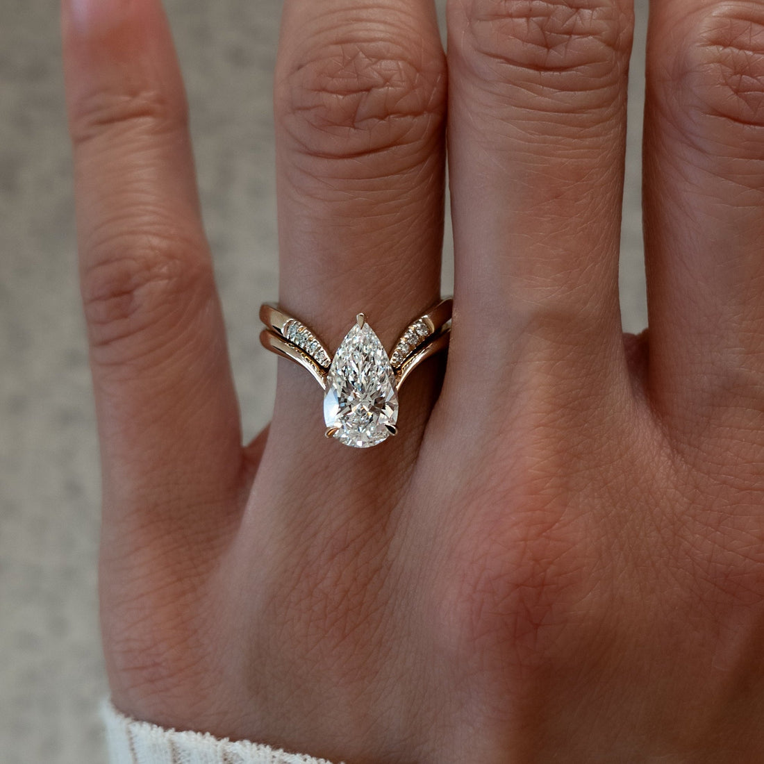 Pear moissanite V shank bridal set with pave-tipped chevron band in yellow gold on the hand