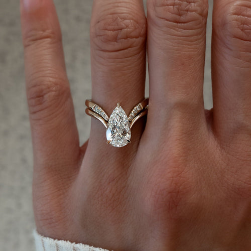 Pear moissanite V shank bridal set with pave-tipped chevron band in yellow gold on the hand