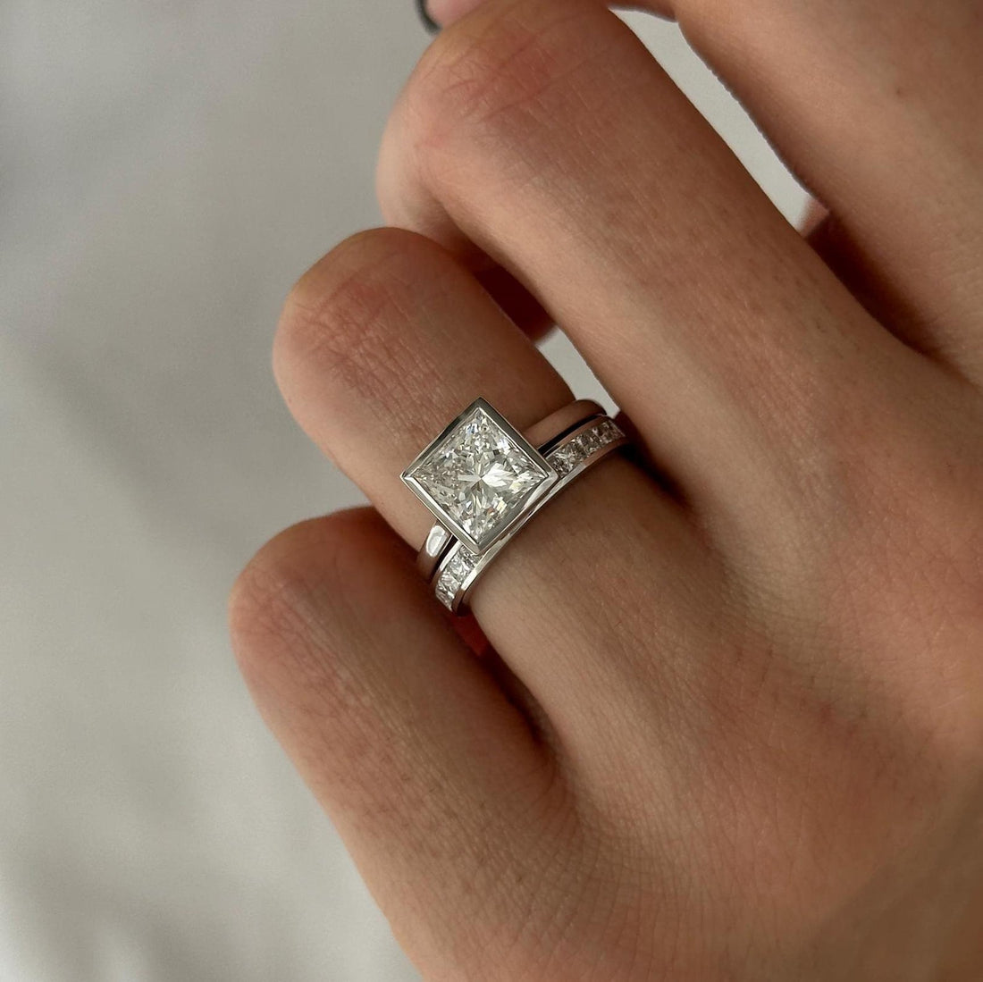 Princess cut moissanite bezel solitaire with channel set princess band in white gold on the hand