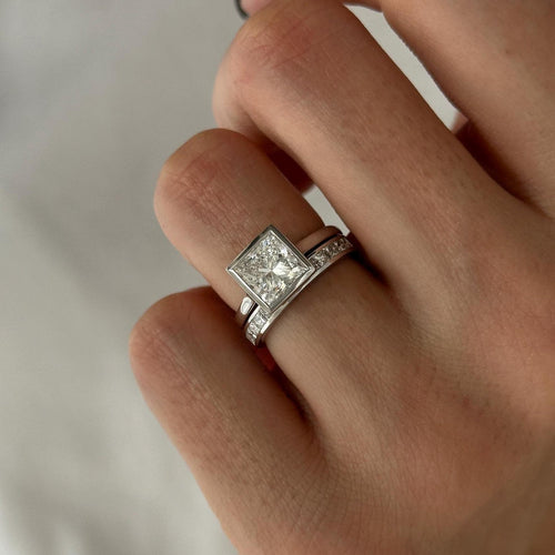 Princess cut moissanite bezel solitaire with channel set princess band in white gold on the hand