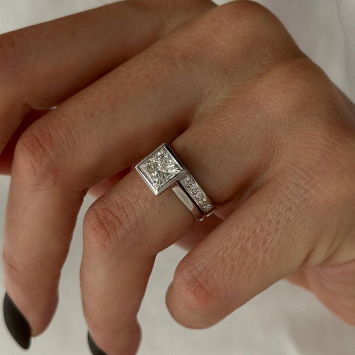 Angled view of princess moissanite square bezel ring and channel set wedding band