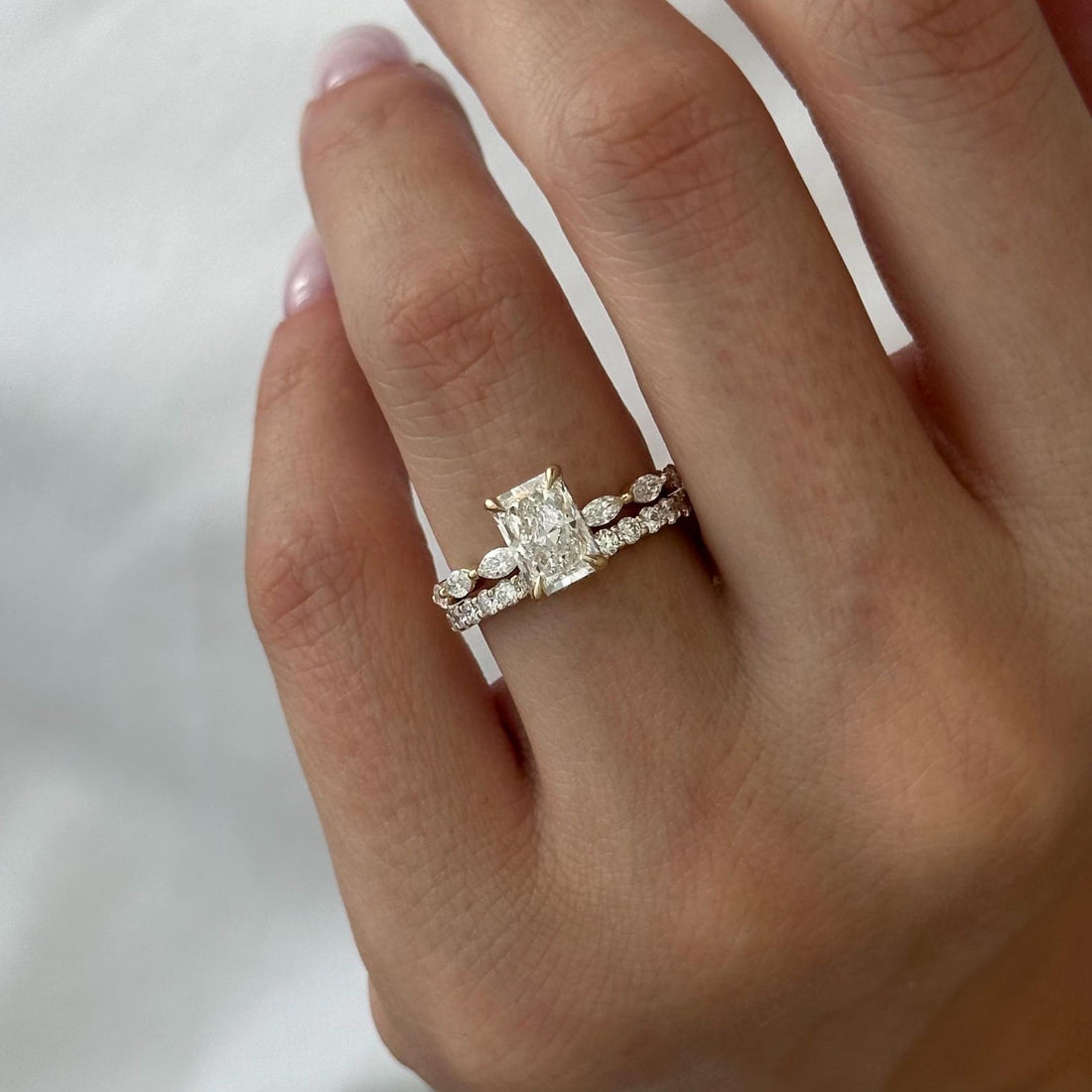 Radiant moissanite marquise station bridal set with round stone band in yellow gold on the hand
