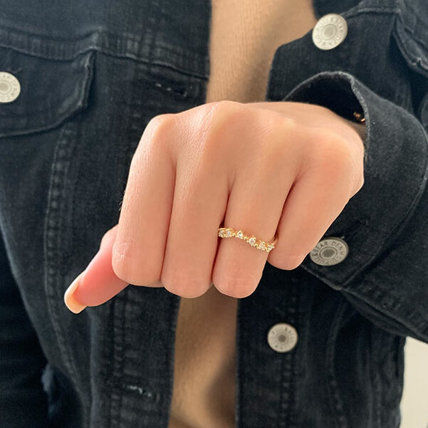 Round moissanite curved wedding band worn on a hand, yellow gold