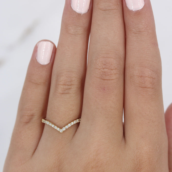 Curved V moissanite wedding band in yellow gold worn on a hand