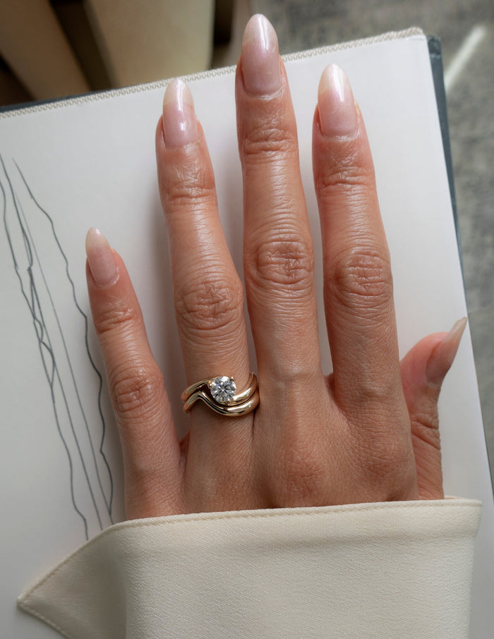 Round lab grown diamond swirl bypass ring and plain gold wave band shown on the full hand