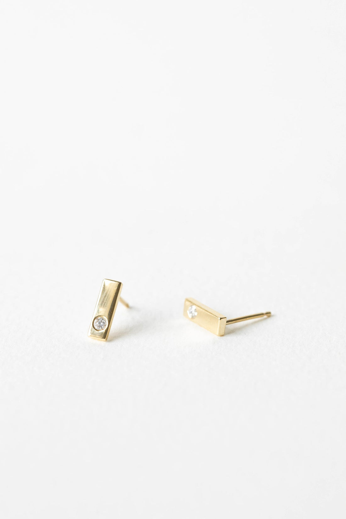 Pair of polished yellow gold bar stud earrings, each flush set with a small round lab grown diamond, on a white background