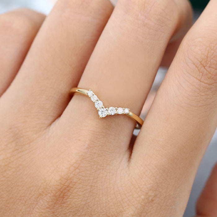 Round moissanite graduated v curved wedding band, worn on the finger in yellow gold