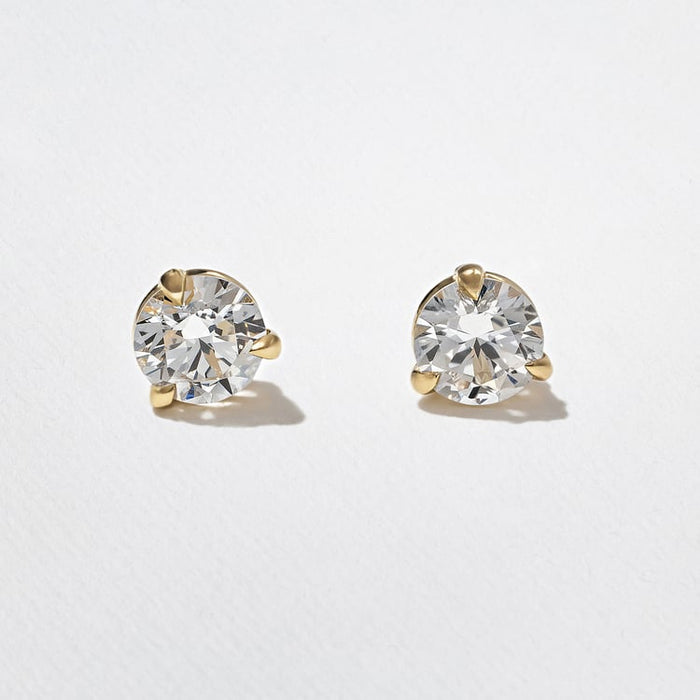 Front view of a pair of round lab grown diamond stud earrings in three prong yellow gold martini settings on textured white paper