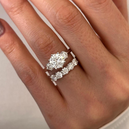Round moissanite three stone bridal set with five stone band in white gold worn on the hand