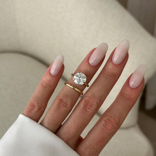 Round moissanite four-prong solitaire and plain domed gold band worn on the hand