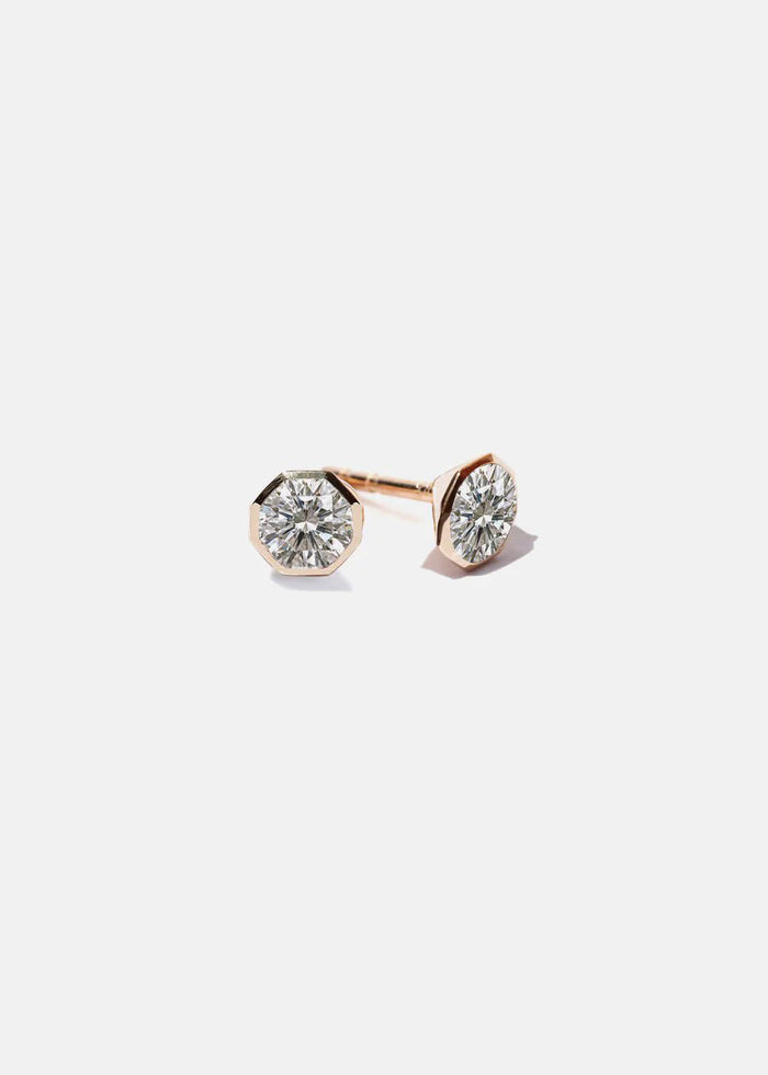 Pair of round lab grown diamond stud earrings in an octagon shaped rose gold bezel on a light grey background