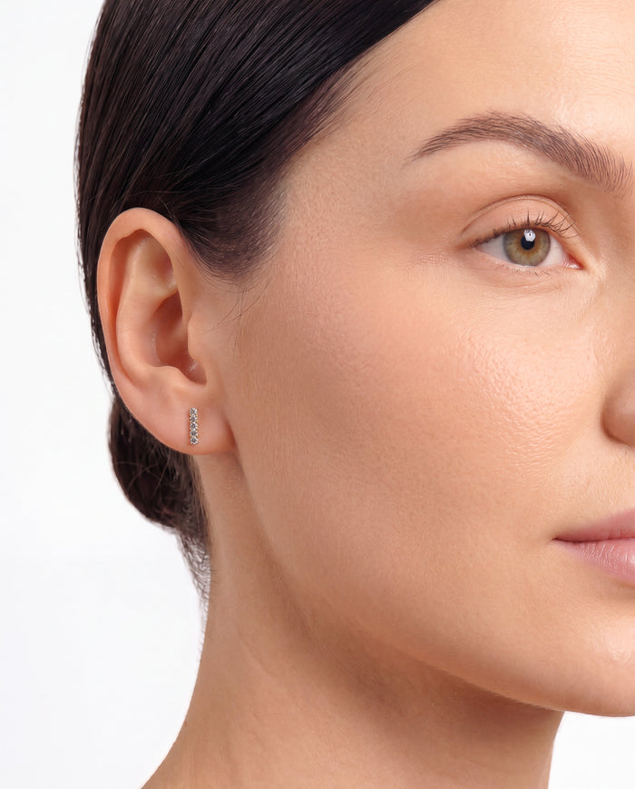 Model wearing round pave bar lab grown diamond stud earrings, close up on the ear