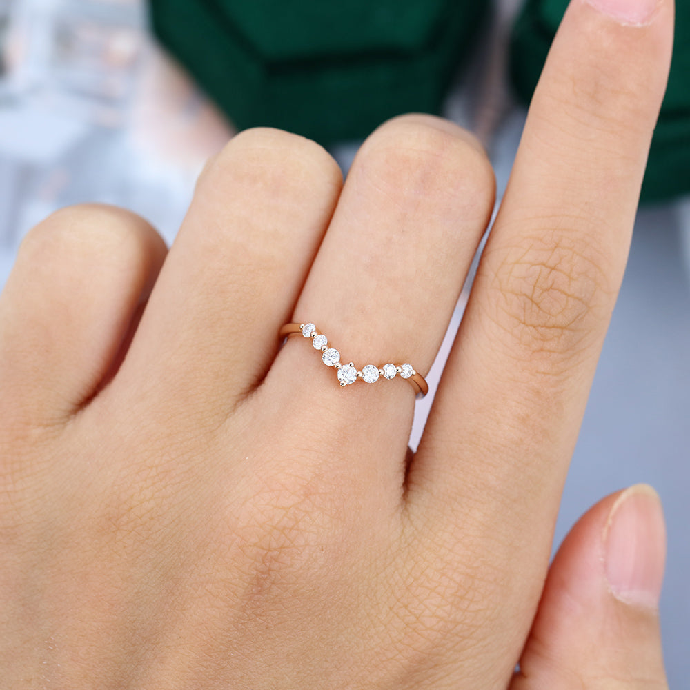 Round moissanite spaced stone v curved wedding band, worn on the finger in rose gold