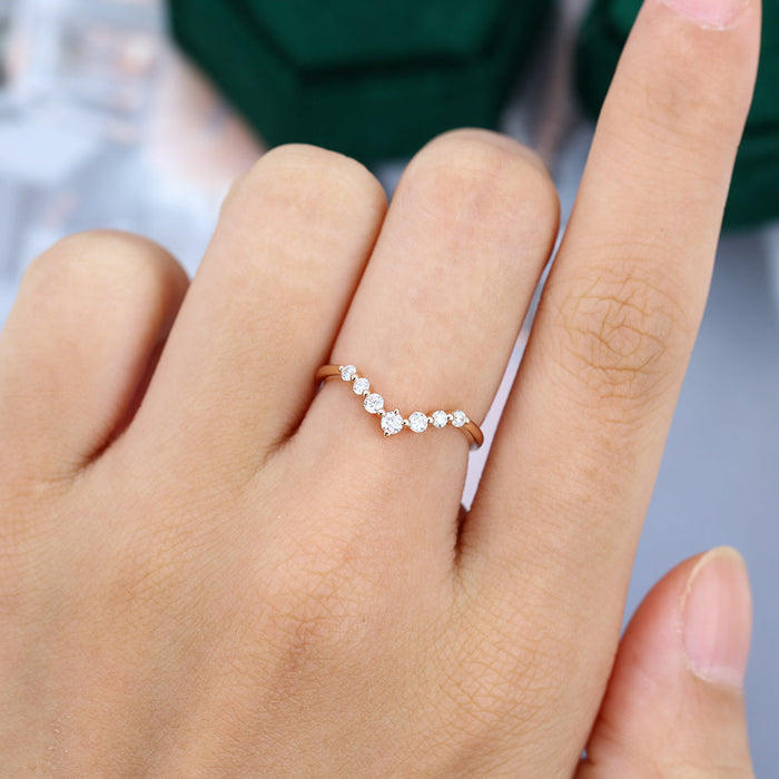 Round moissanite spaced stone v curved wedding band, worn on the finger in rose gold